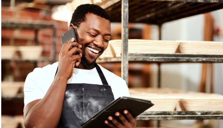 Cropped shot of a male baker talking on the phone while using a digital tablet at work